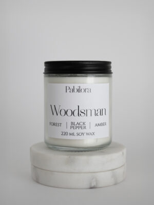Pabilora Woodsman scented candle in a glass jar blending forest freshness, spicy black pepper, and warm amber notes.