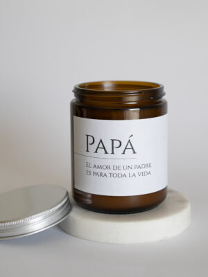 "Papá" scented candle in a glass jar, featuring warm sandalwood, exotic saffron, cedar, clove, amber, musk, and vanilla notes, evoking love and protection across generations.